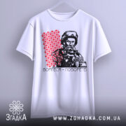 Футболка борітеся поборете, білого кольору, зображена на вішалці, фон світло-сірий, принт з червоним орнаментом та чорно-білим зображенням чоловіка в військовій формі.