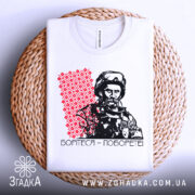 Футболка борітеся поборете, білого кольору, зображена на плетеній кошику, фон білий, принт з червоним орнаментом та чорно-білим зображенням чоловіка в військовій формі.