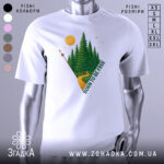 Футболка born free білого кольору, зображена на манекені, з принтом лісу, дороги та сонця, ракурс спереду, фон світло-сірий.