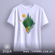 Футболка born free білого кольору, підвішена на вішалці, з принтом лісу, дороги та сонця, ракурс спереду, фон світло-сірий.