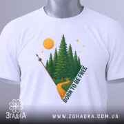 Футболка born free білого кольору, складена на поверхні, з принтом лісу, дороги та сонця, вид зверху, фон світло-сірий.