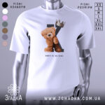 Футболка born king, білого кольору, зображена на манекені з блискучою поверхнею, фон світло-сірий, принт з ведмедиком та короною на літері K, текст 'BORN TO BE KING' під малюнком.