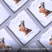 Футболка born king, білого кольору, зображена на манекені з блискучою поверхнею, фон світло-сірий, принт з ведмедиком та короною на літері K, текст 'BORN TO BE KING' під малюнком.