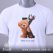 Футболка born king, білого кольору, складена на столі, фон світло-сірий, принт з ведмедиком та короною на літері K, текст 'BORN TO BE KING' під малюнком, на футболці є етикетка з зеленим шнурком.