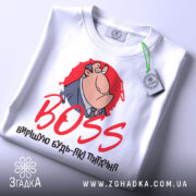 Футболка бос вирішую питання. Біла футболка, зображена зверху, принт з персонажем в костюмі на червоному фоні, текст 'BOSS' червоним шрифтом, на футболці є етикетка з зеленим шнурком.