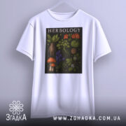 Футболка ботанічний арт, біла, підвішена на вішалці, фон світло-сірий, принт з рослинами та грибами, текст 'HERBOLOGY' на чорному фоні.