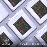 Футболка ботанічний арт, біла, зображена на манекені, фон світло-сірий, принт містить різноманітні рослини, гриби та текст 'HERBOLOGY' на чорному фоні.