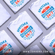 Футболка братська підтримка, біла, зображена з правого боку на манекені, фон нейтральний, принт містить червоні та блакитні елементи з написом 'Братська підтримка 24/7' та зображенням з'єднаних кулаків.