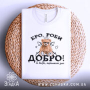 Футболка бро роби добро, біла, складена на плетеній кошику, фон світлий, принт з ведмедиком у короні, напис 'ДОБРО!' з елементами сердець і стріл.