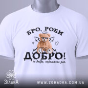 Футболка бро роби добро, біла, складена на столі, фон світлий, принт з ведмедиком у короні, напис 'ДОБРО!' з елементами сердець і стріл.