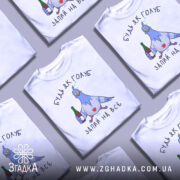 Футболка будь як голуб, білого кольору, зображена з фронтального ракурсу на манекені, фон світло-сірий, принт з веселим голубом, який тримає пляшку та келих, текст "ЗАПИЙ НА ВСЕ".