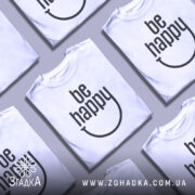 Футболка будь щасливим, білого кольору, зображена з близького ракурсу на манекені, фон світло-сірий, принт чорного кольору з написом 'be happy' і усмішкою.