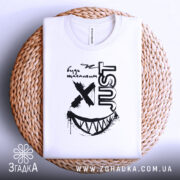 Футболка будь щасливим, біла, складена на плетеній основі, фон світло-сірий, принт чорного кольору з усмішкою та написом 'JUST'.