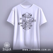 Футболка будь собою, біла, зображена з фронтального ракурсу, підвішена на вішалці, фон світло-сірий, принт чорного кольору з написом 'Будь собою' та 'Інші ролі вже зайняті', оформлений у стилі вензелів.