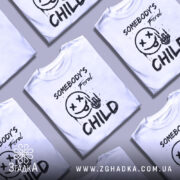 Футболка бунтівна дитина, біла, зображена з фронтального ракурсу, фон нейтральний, принт містить смайлик з хрестиками на очах, язиком та рукою з черепом, текст 'SOMEBODY'S Feral CHILD' виконаний у чорному кольорі.