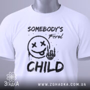 Футболка бунтівна дитина, біла, зображена зверху, на ній видно етикетку з зеленим шнурком, фон світлий, принт аналогічний попередньому, текст та малюнок виконані в чорному кольорі.