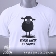 Футболка бути іншим. Біла футболка, складена на столі, з принтом чорної овечки, зображено зверху. Принт чітко видимий, текст "BLACK SHEEP BY CHOICE" розташований під овечкою. На футболці є етикетка з зеленим шнурком.