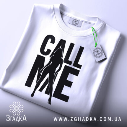 Футболка call me білого кольору, складена на столі, фон світло-сірий, принт чорного кольору з силуетом жінки та написом 'CALL ME', на комірці видна етикетка.