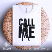Футболка call me білого кольору, складена на плетеній кошику, фон світло-сірий, принт чорного кольору з силуетом жінки та написом 'CALL ME'.