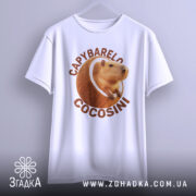 Футболка Capybarelo Cocosini білого кольору, зображена на вішалці, фон світло-сірий, принт з капібарою в кокосі розташований по центру, виглядає яскраво.