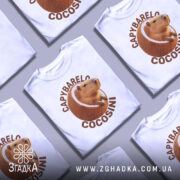 Футболка Capybarelo Cocosini білого кольору, зображена з правого ракурсу на манекені, фон світло-сірий, принт з капібарою в кокосі виконаний у натуральних кольорах.