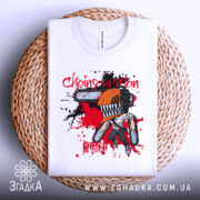 Футболка Chainsaw Man білого кольору, складена на плетеній основі, зображена з верхнього ракурсу, фон натуральний, принт з персонажем з бензопилою, оранжевий шолом, червоні та чорні плями навколо.