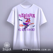 Футболка чарівна на голову, біла, показана з фронтального ракурсу на нейтральному фоні, принт з чарівницею на мітлі з червоним волоссям і летючими кажанами, текст 'Чарівна на всю голову' в фіолетовому кольорі.