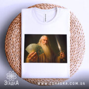 Футболка чарівник з доларами, біла, складена на плетеній основі, фон білий, принт зображає чоловіка з довгим волоссям і бородою, який тримає гроші і меч.