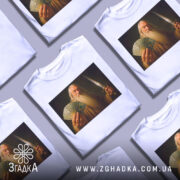 Футболка чарівник з доларами, біла, зображена на манекені, фон світло-сірий, принт зображає чоловіка з довгим волоссям і бородою, який тримає гроші і меч.