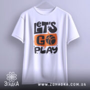 Футболка час грати баскетбол, біла футболка, підвішена на вішалці, з принтом 'LET'S GO PLAY' в оранжевому та чорному кольорах, фон світло-сірий, футболка виглядає стильно.