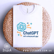 Футболка ChatGPT мій друг, біла, складена на плетеній тарілці, фон світло-сірий, принт з логотипом ChatGPT у блакитному та оранжевому кольорах.