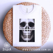 Футболка череп модний принт, біла, складена на плетеній кошику, фон світло-сірий, принт зображає череп у чотирьох квадратах, деталі принта чіткі та контрастні.