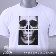 Футболка череп модний принт, біла, складена на поверхні, фон світло-сірий, принт зображає череп у чотирьох квадратах, на футболці є етикетка з зеленим шнурком.
