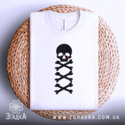 Футболка череп символ, біла, складена на плетеній кошику, фон світлий, принт чорного черепа з червоною краплею та кістками.