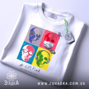 Футболка черепи рок стиль, біла, розкладена на поверхні, фон світло-сірий, принт з чотирьох черепів у кольорових квадратах, текст '# Let's Rock' під принтом, на комірці видна етикетка.