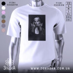 Футболка черниця тату білого кольору, зображена на манекені з блискучим металевим покриттям, фон світло-сірий, принт з чорно-білою фотографією дівчини в чернечому вбранні з татуюваннями на руках.