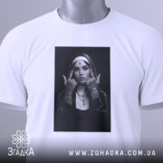 Футболка черниця тату білого кольору, складена на поверхні з легким відблиском, фон світло-сірий, принт з чорно-білою фотографією дівчини в чернечому вбранні, на футболці є етикетка з зеленим шнурком.