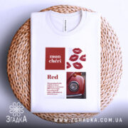 Футболка червоний акцент, біла футболка з принтом, зображена зверху на плетеній основі, фон світлий, принт містить червоні губи та зображення червоного автомобіля.