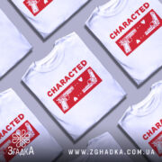 Футболка червоний стиль, біла футболка на манекені, з принтом червоного кольору, на якому зображені два пістолети та напис 'CHARACTED', фон світло-сірий, акцент на принті.