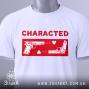 Футболка червоний стиль, складена біла футболка з принтом червоного кольору, на якому зображені два пістолети та напис 'CHARACTED', фон світло-сірий, видно етикетку з зеленим шнурком.