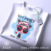 Футболка чого дивишся? Біла футболка, зображена зверху, з принтом дівчинки в червоних окулярах, фон світло-сірий, на комірці видно етикетку.