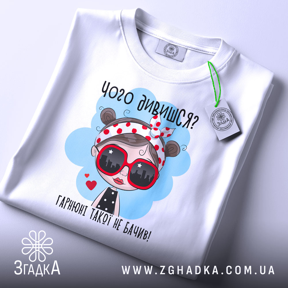 Футболка чого дивишся? Біла футболка, зображена зверху, з принтом дівчинки в червоних окулярах, фон світло-сірий, на комірці видно етикетку.