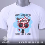 Футболка чого дивишся? Біла футболка, зображена зверху, з принтом дівчинки в червоних окулярах, фон світло-сірий, на комірці видно етикетку.