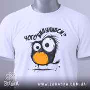 Футболка чого вилупився, білого кольору, складена на поверхні, фон світлий, принт з пташеням з великими очима та оранжевим животом, на футболці є етикетка.