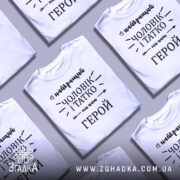 Футболка чоловік і татко, біла, зображена з фронтального ракурсу на манекені, фон світло-сірий, принт чорного кольору з написом 'найкращий чоловік і татко ми наш герой'.