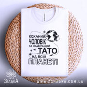 Футболка чоловік тато білого кольору, зображена зверху на плетеній основі, фон світлий, принт чорного кольору з текстом "Коханий чоловік та найкращий Тато на всій планеті".