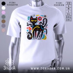 Футболка чорний кіт на білому фоні, зображена з фронтального ракурсу, на манекені, принт з абстрактним чорним котом з жовтими очима та кольоровими геометричними елементами.