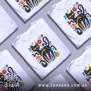 Футболка чорний кіт на білому фоні, зображена з фронтального ракурсу, на манекені, принт з абстрактним чорним котом з жовтими очима та кольоровими геометричними елементами.