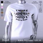 Футболка чудова донечка, біла, зображена на манекені з правого боку, фон світло-сірий, принт чорного кольору з жовтими зірками та різними символами, текст українською мовою.