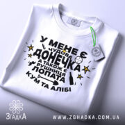 Футболка чудова донечка, біла, зображена зверху, фон світло-сірий, принт чорного кольору з жовтими зірками, текст українською мовою, на комірці є етикетка.